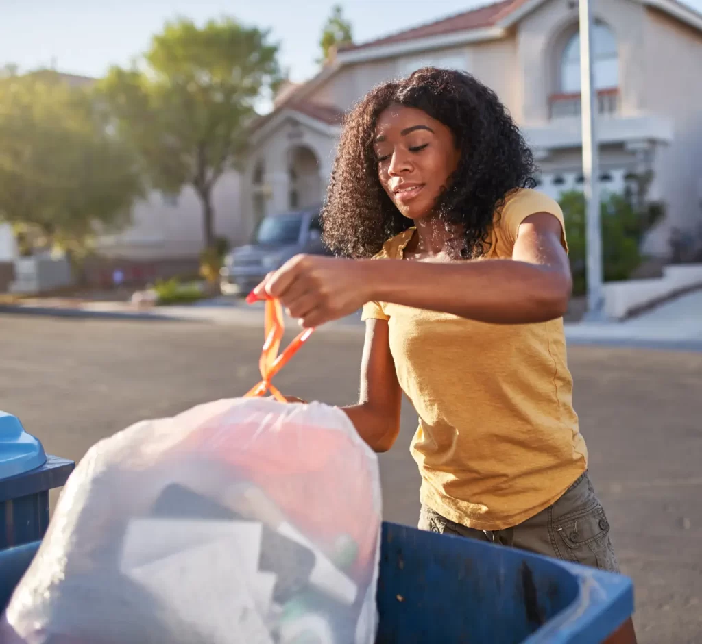 Young woman throwing away trash in residential curbside trash can.